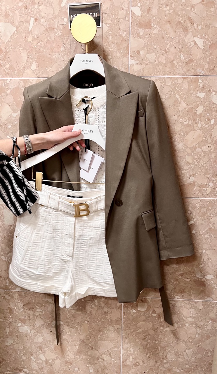 Outfit Kombination auf Kleiderständer mit cremefarbenem Top mit Shorts, und olivfarbenem Blazer vor roséfarbener Marmor Wand